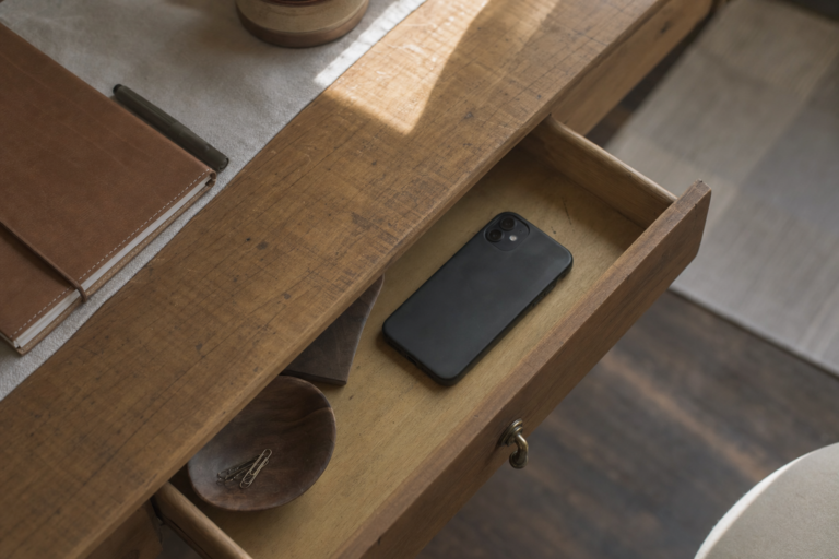 Smartphone set aside in a wooden drawer beside a journal, symbolizing a break from constant notifications
