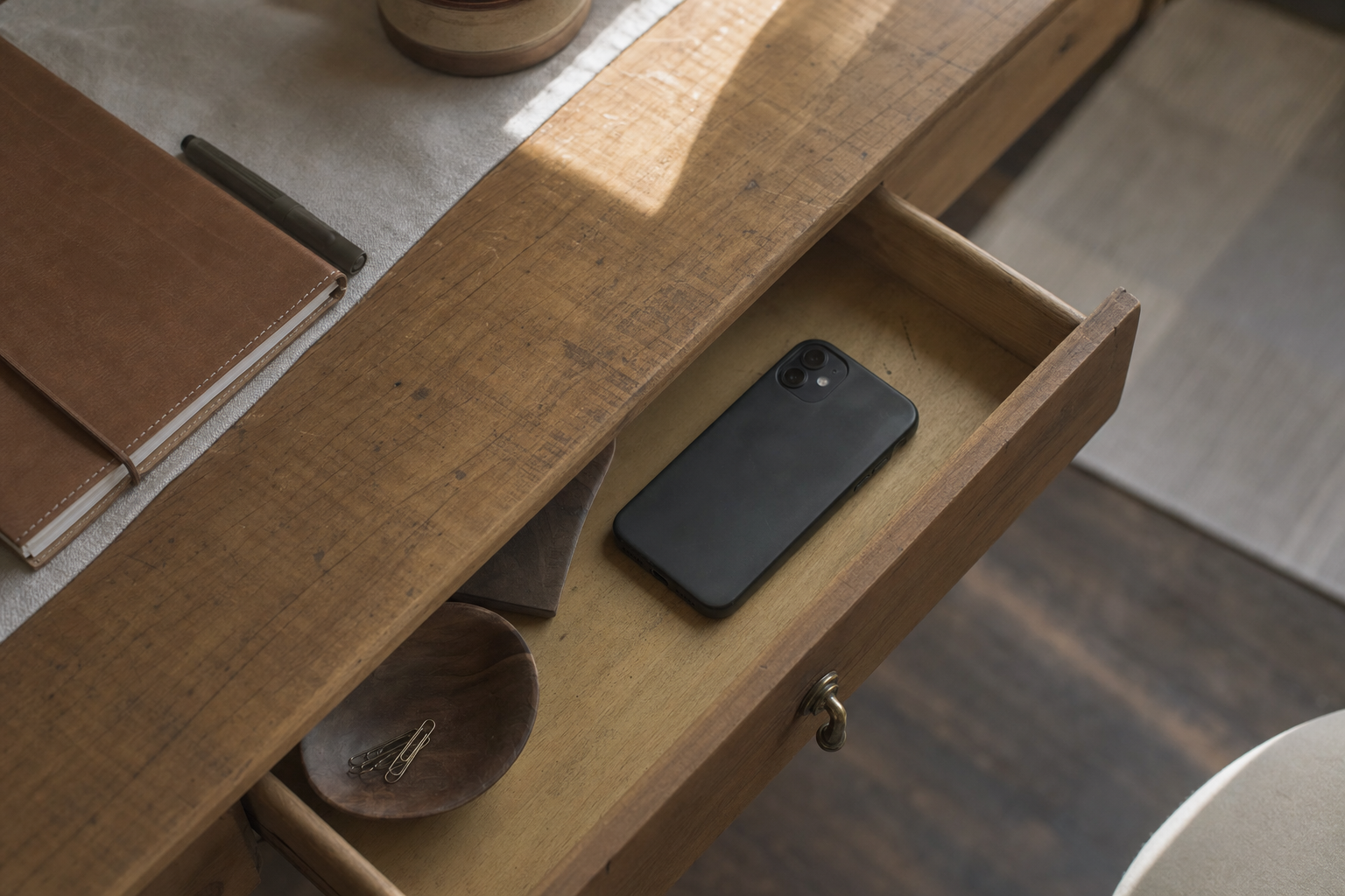 Smartphone set aside in a wooden drawer beside a journal, symbolizing a break from constant notifications