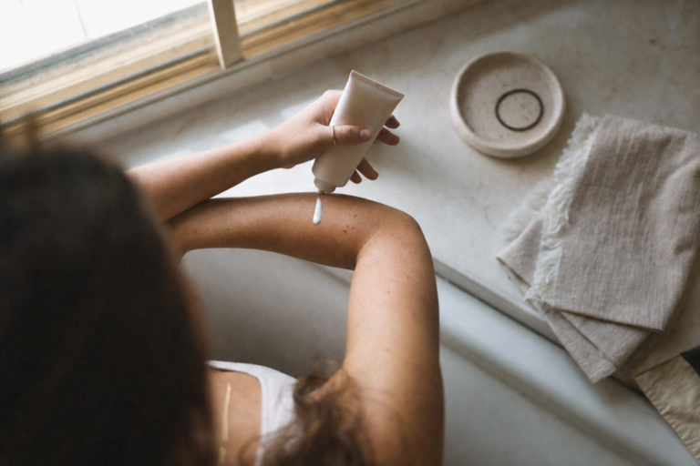 Hands applying sunscreen in soft morning bathroom light as part of a daily skin longevity habit