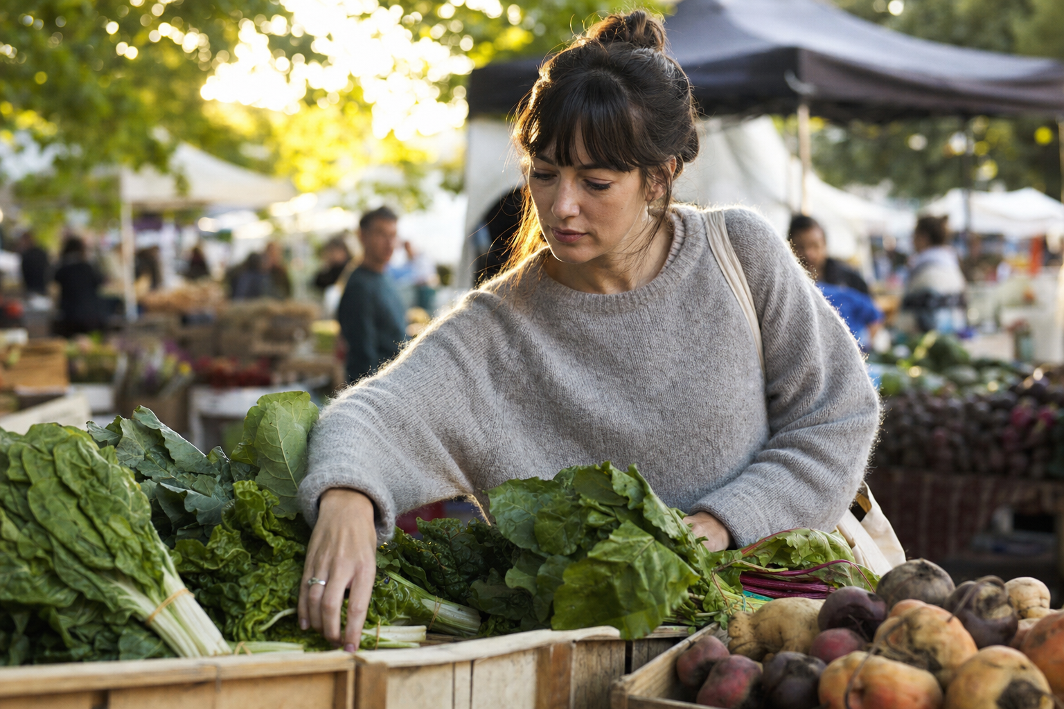 Person choosing fresh vegetables at a farmers market stall in golden hour light