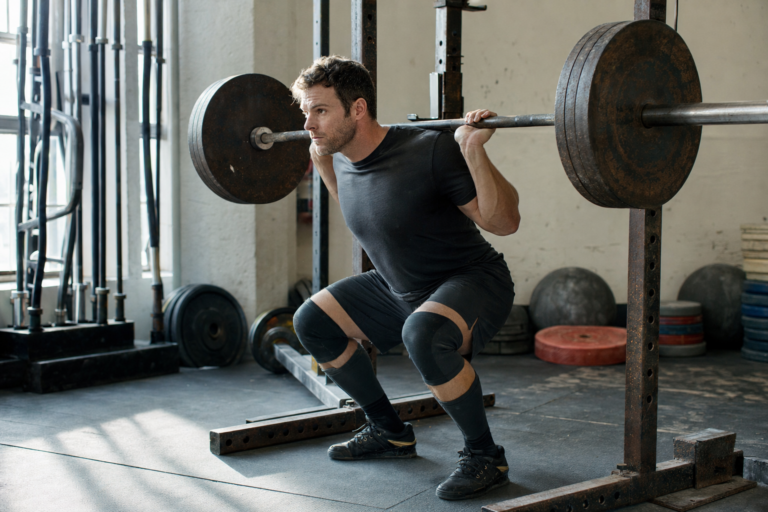 Lifter mid-set on a barbell rack in a sunlit independent gym