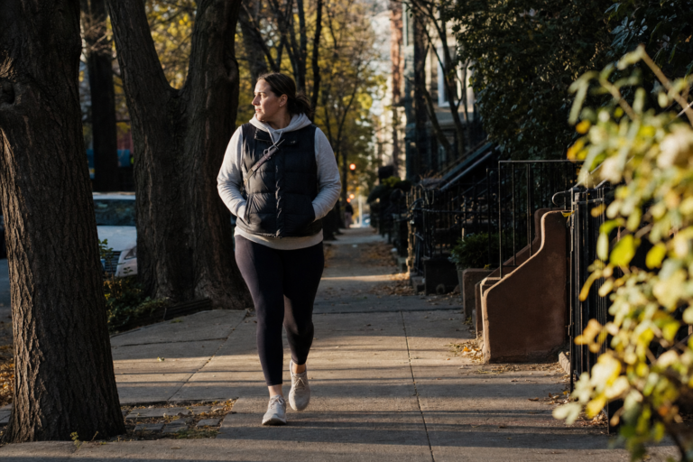 Person walking briskly along a tree-lined sidewalk in warm afternoon light